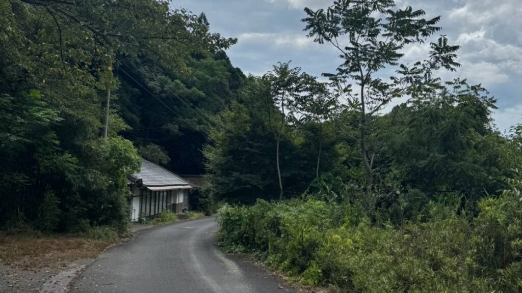 山あいの細い舗装路沿いに建つ古い平屋