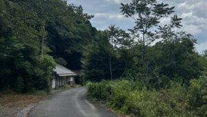山あいの細い舗装路沿いに建つ古い平屋