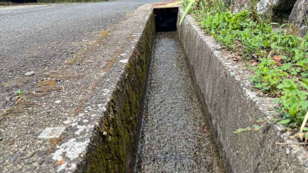 道路脇に続くコンクリート側溝と岩の擁壁